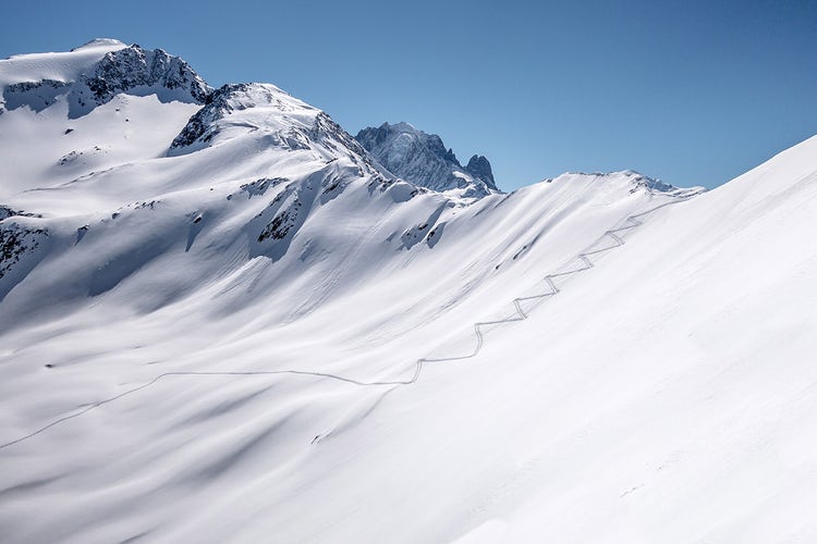Ski touring track leading up alpine mountain slope to ridge and pass in untouched powder snow in winter
